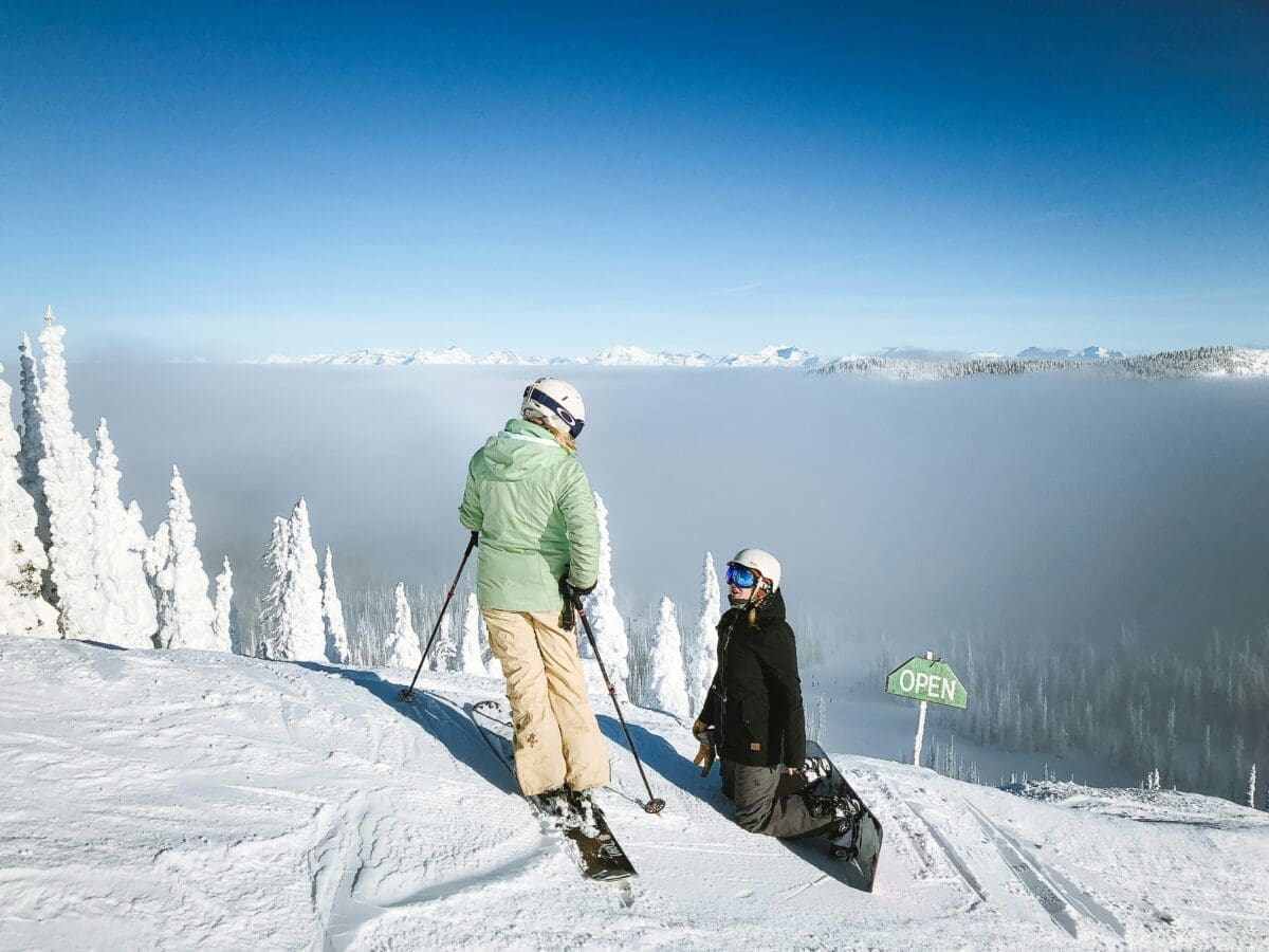 a skiier and a snowboarder rendezvous at the top of a mountain skiing vs snowboarding featured image